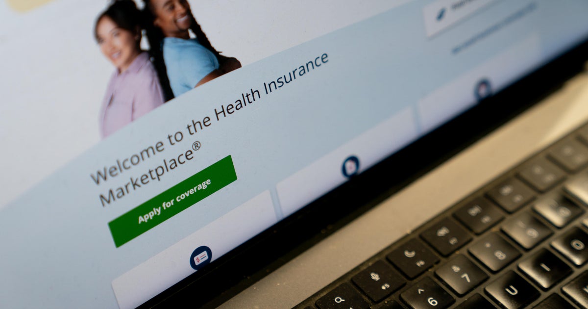 A person reviews a 2026 ACA marketplace health insurance renewal notice showing a sharply higher monthly premium at a kitchen table