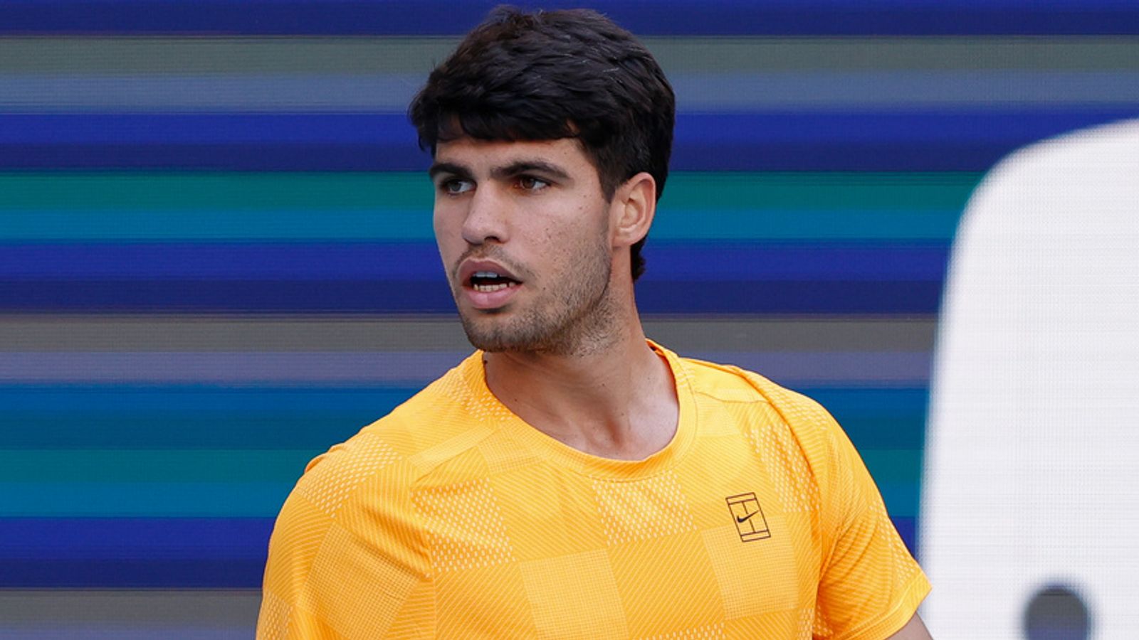 Carlos Alcaraz grimacing and holding his right wrist during a tennis match on court