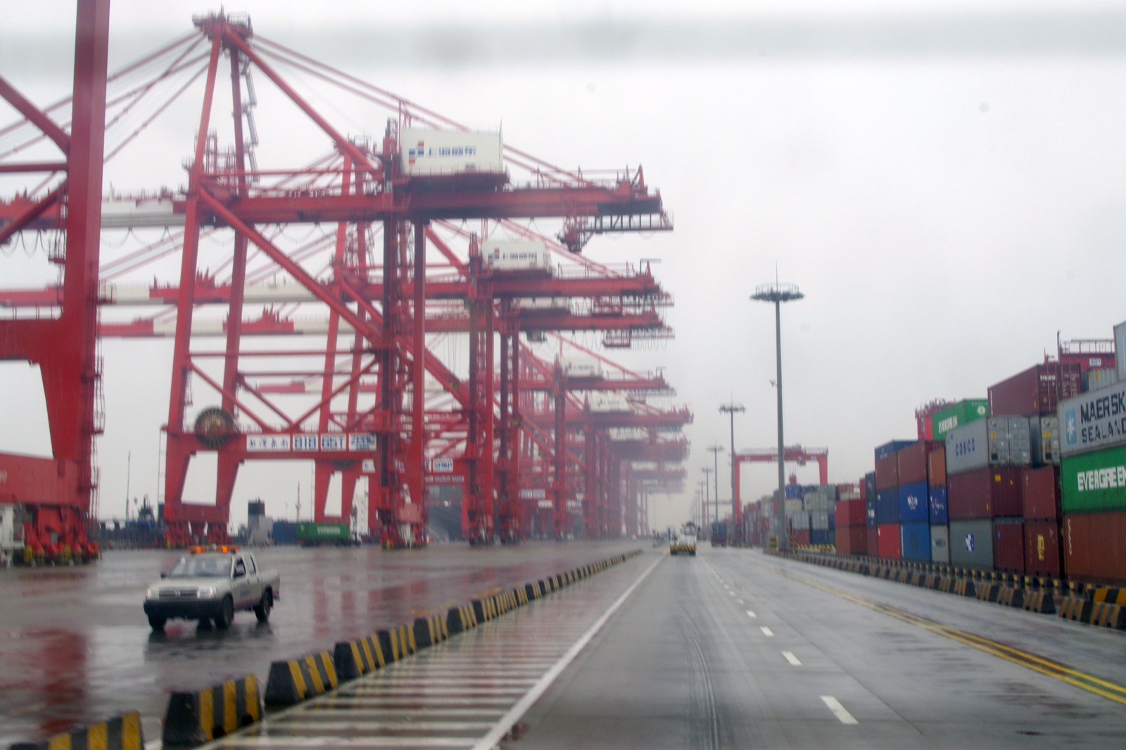 Container cranes and stacked shipping containers at Yangshan deep-water port near Shanghai, the export gateway sustaining Chinese factory earnings. Photo: Acstar / Wikimedia Commons, CC0.