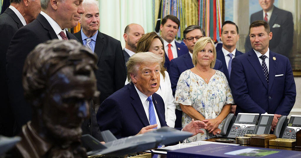 President Trump signing the Secure America Act at the Resolute Desk in the Oval Office as House Speaker Mike Johnson and DHS Secretary Markwayne Mullin look on