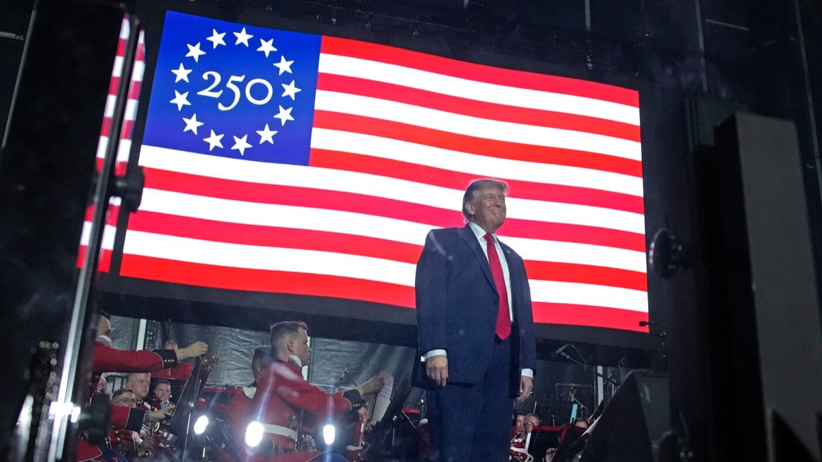 President Donald Trump on stage before a 250-star anniversary flag at an America250 event. Source: NPR